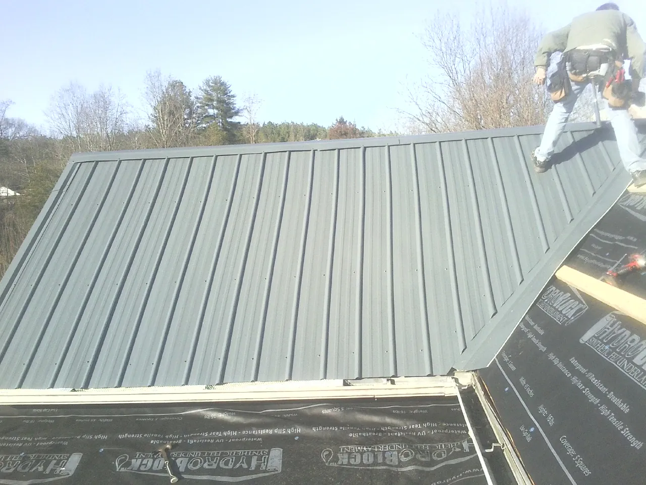 Crew installing dark green standing seam panels over synthetic underlayment in Harper