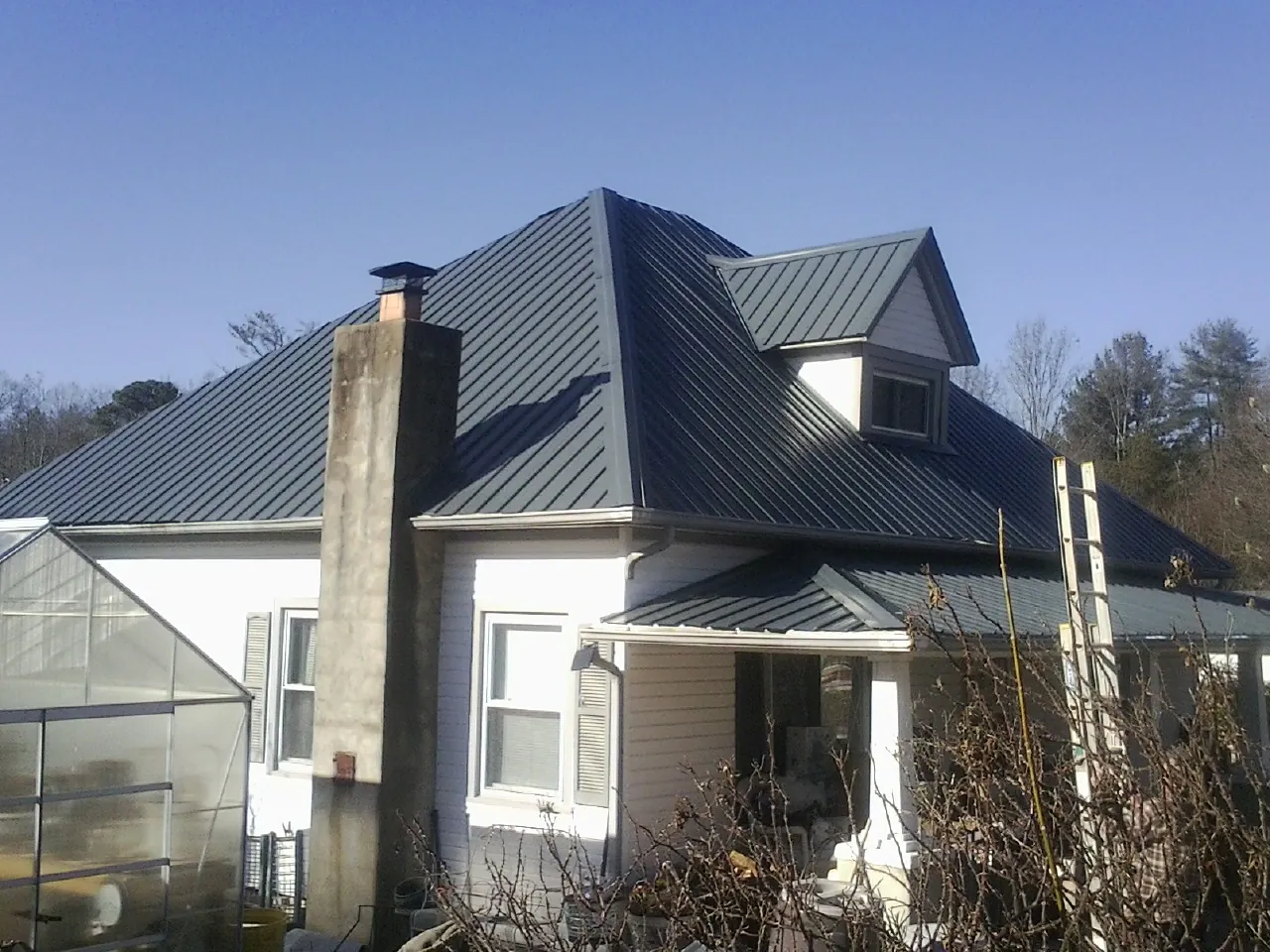 Dark blue standing seam metal roof on a white farmhouse with dormer — Slate & Tile Roof Repair by Roofing Brothers in Harper