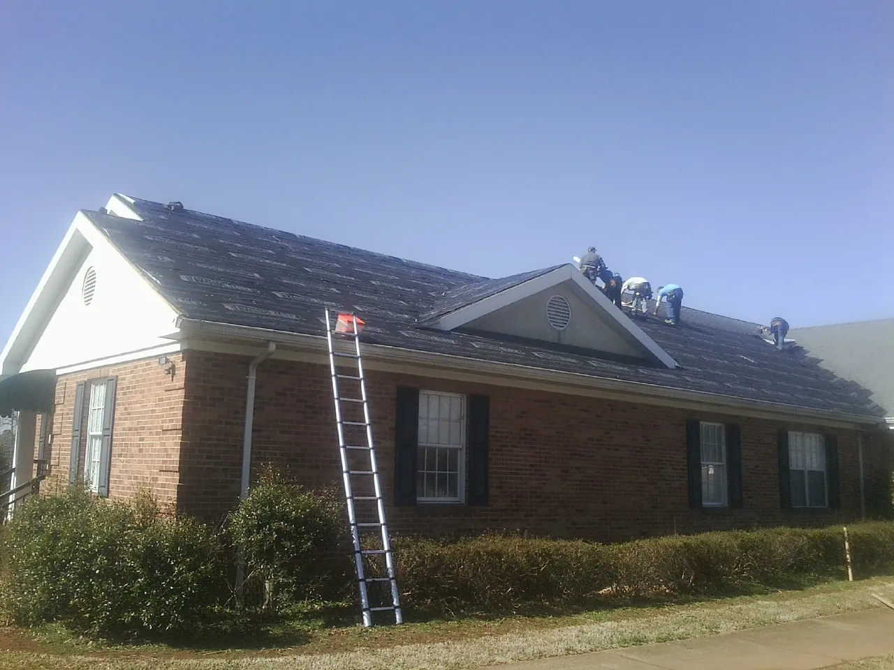 Crew tearing shingles off a brick ranch roof with a ladder set — Metal Roof Repair work by our crew in Harper