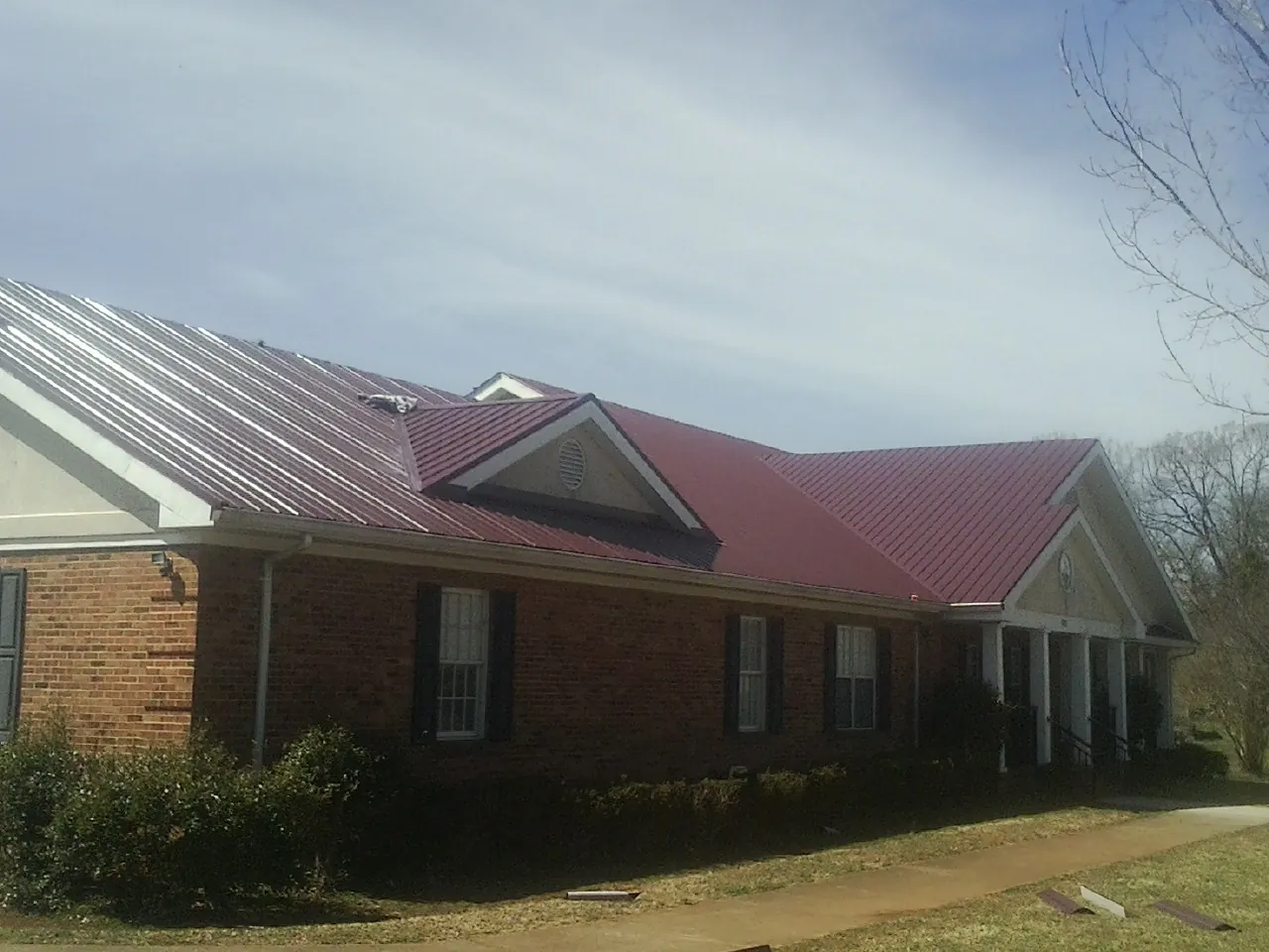 Red metal roof with gabled entries on a long brick building, from a Hail Damage Roof Repair job in Harper
