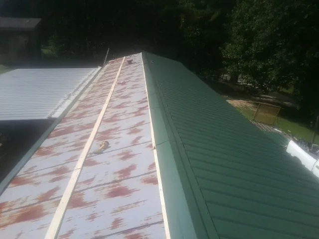 Old rusted panels beside newly installed green metal roofing — Wind Damage Roof Repair by Roofing Brothers in Harper