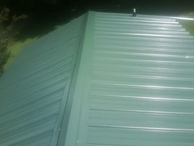 New green metal panels meeting at the ridge of a roof — Flat Roof Repair work by our crew in Harper