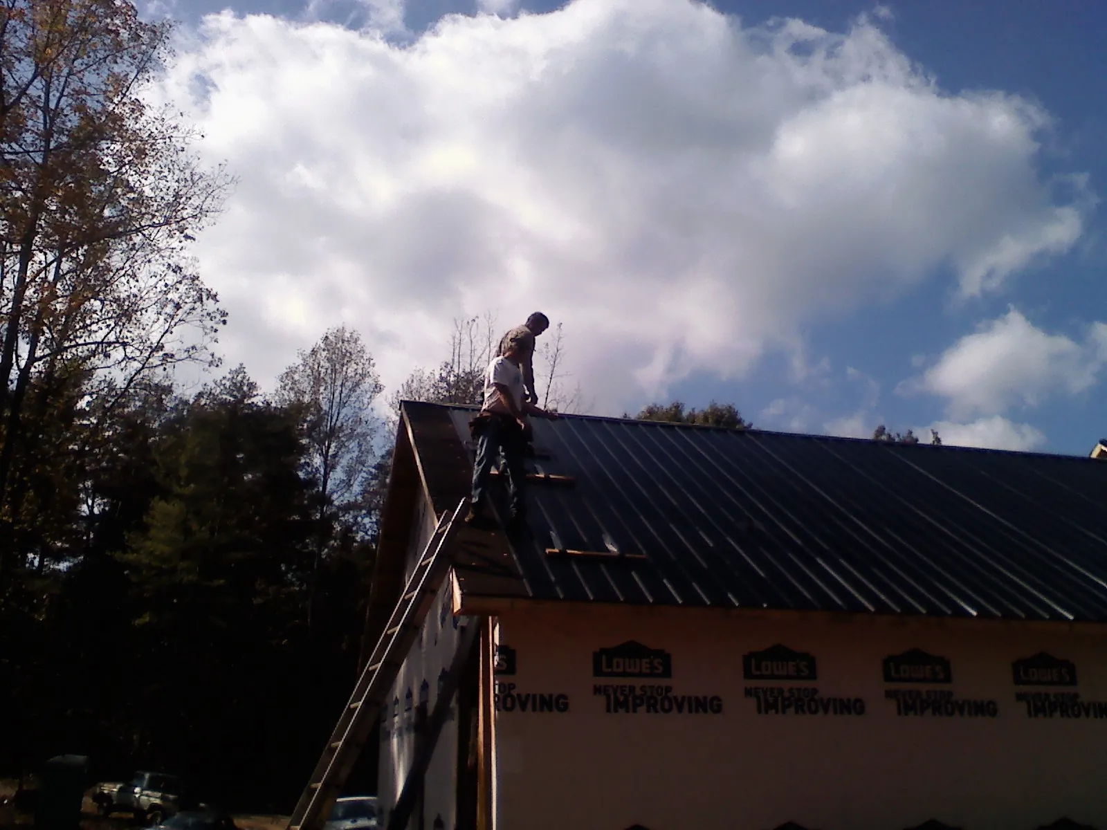 Roofer fastening dark metal panels high against a cloudy sky, from a Roof Inspection job in Harper
