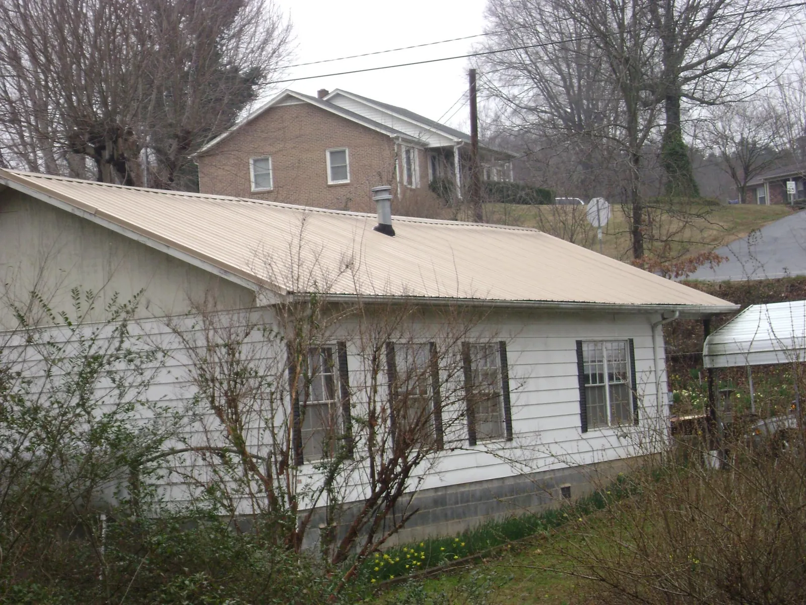 Tan metal roof on a white sided house set into a hillside — Commercial Roofing by Roofing Brothers in Harper