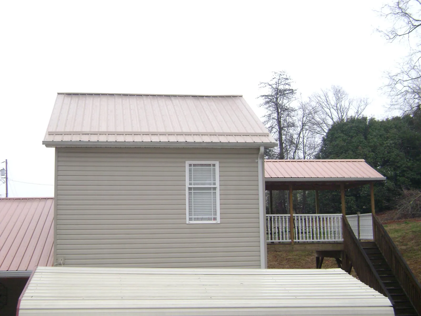Tan metal roofs on a two story addition and attached porch, from a Roof Replacement job in Harper